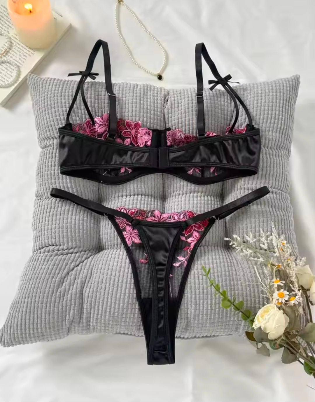 Black lingerie set with pink floral embroidery on a gray pillow.