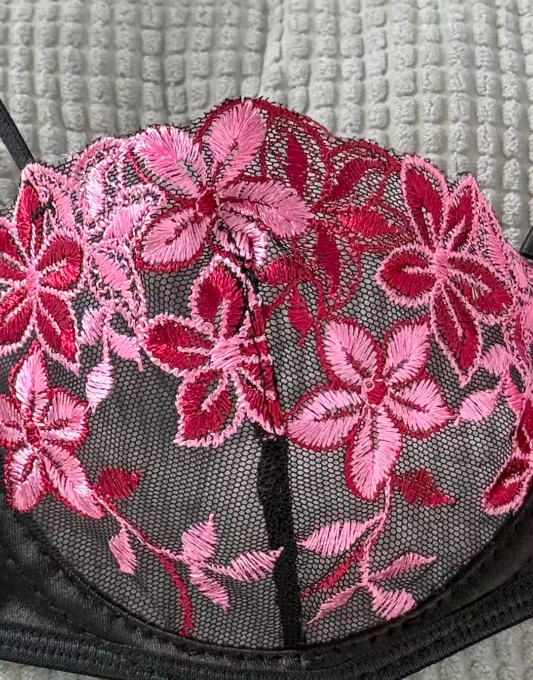 Black bra with pink floral embroidery on a textured gray background