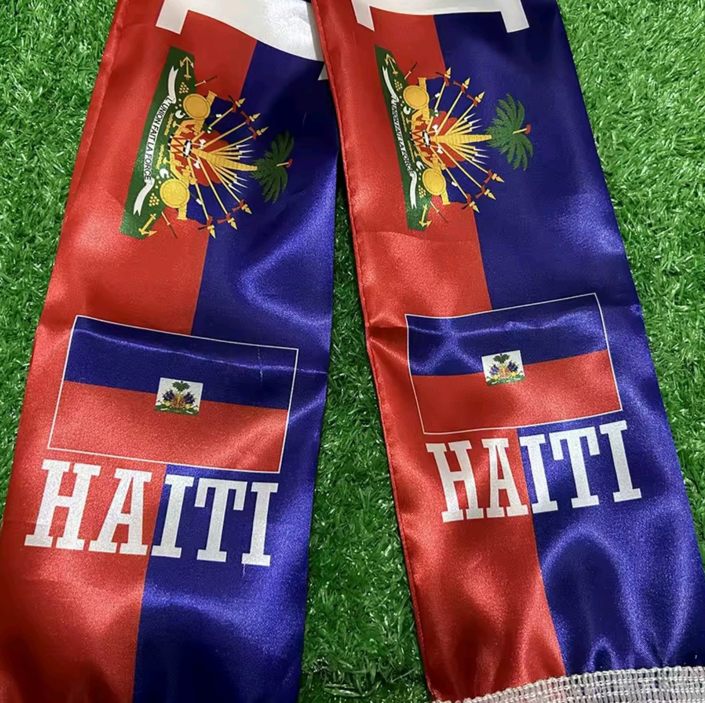 Two red and blue scarves with Haiti text and emblem on a grass background