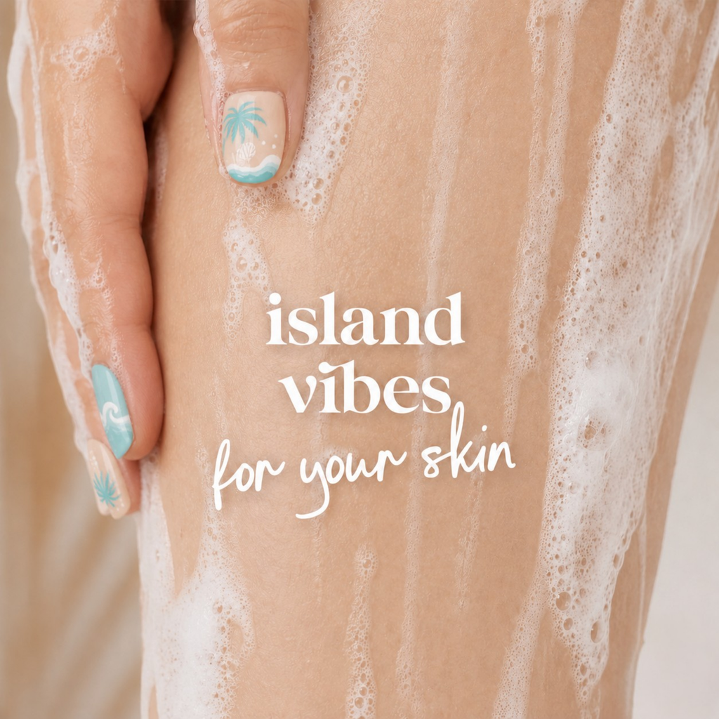 A close-up of a hand with light blue and white nail art resting on a leg covered in white soap foam, with the text 'island vibes for your skin' overlaid in white script.
