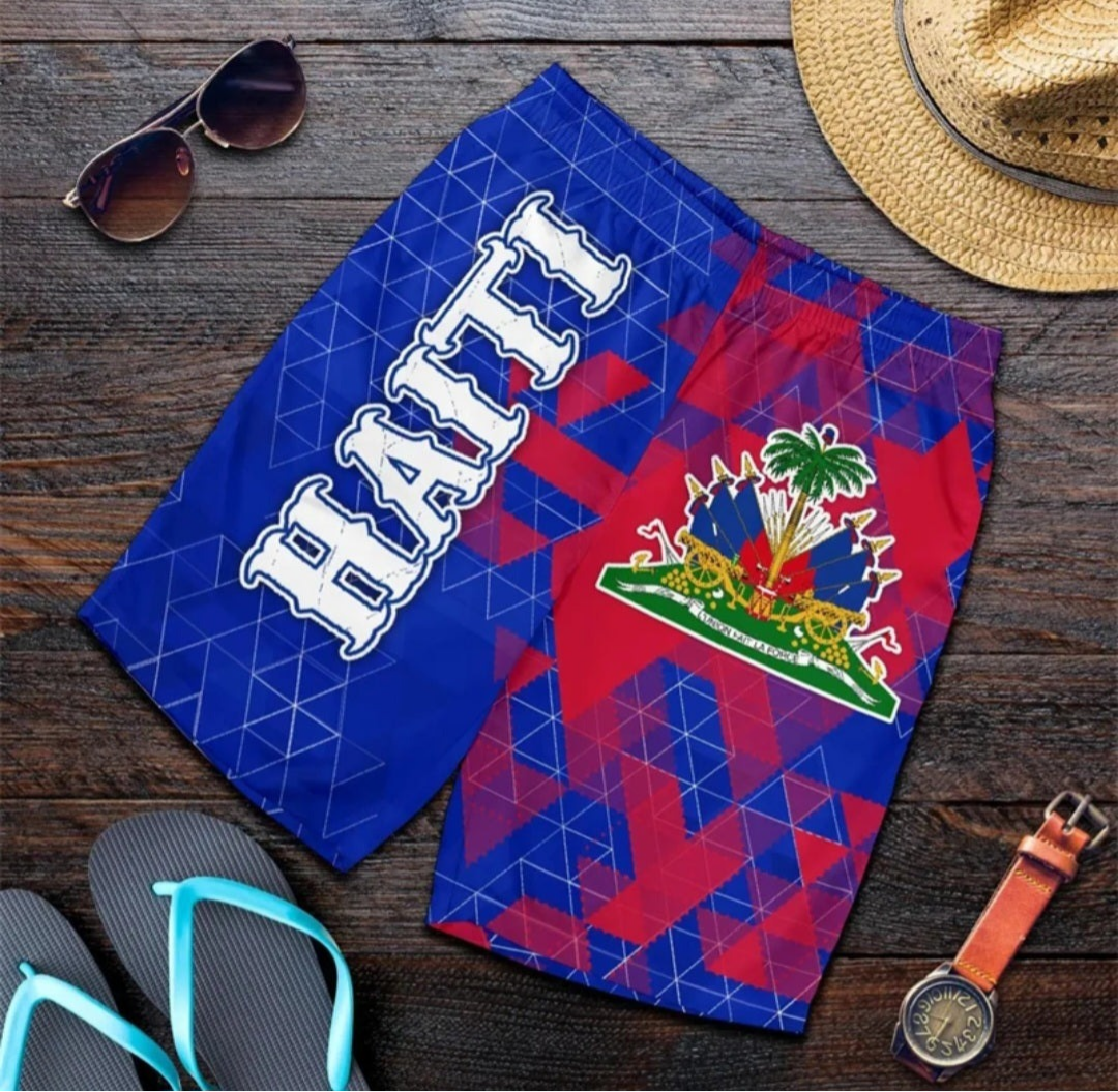 Shorts with a geometric pattern and 'Haiti' text on a wooden surface, surrounded by sunglasses, a hat, flip-flops, and a watch.