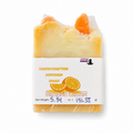 A handcrafted artisan soap bar wrapped in clear plastic, featuring a white paper label that reads 'HANDCRAFTED ARTISAN SOAP ORANGE CREAM' with orange slice graphics. The soap itself is a pale creamy yellow with orange gourd accents on top, set against a plain white background.