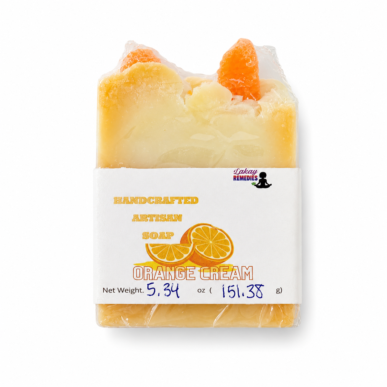 A handcrafted artisan soap bar wrapped in clear plastic, featuring a white paper label that reads 'HANDCRAFTED ARTISAN SOAP ORANGE CREAM' with orange slice graphics. The soap itself is a pale creamy yellow with orange gourd accents on top, set against a plain white background.