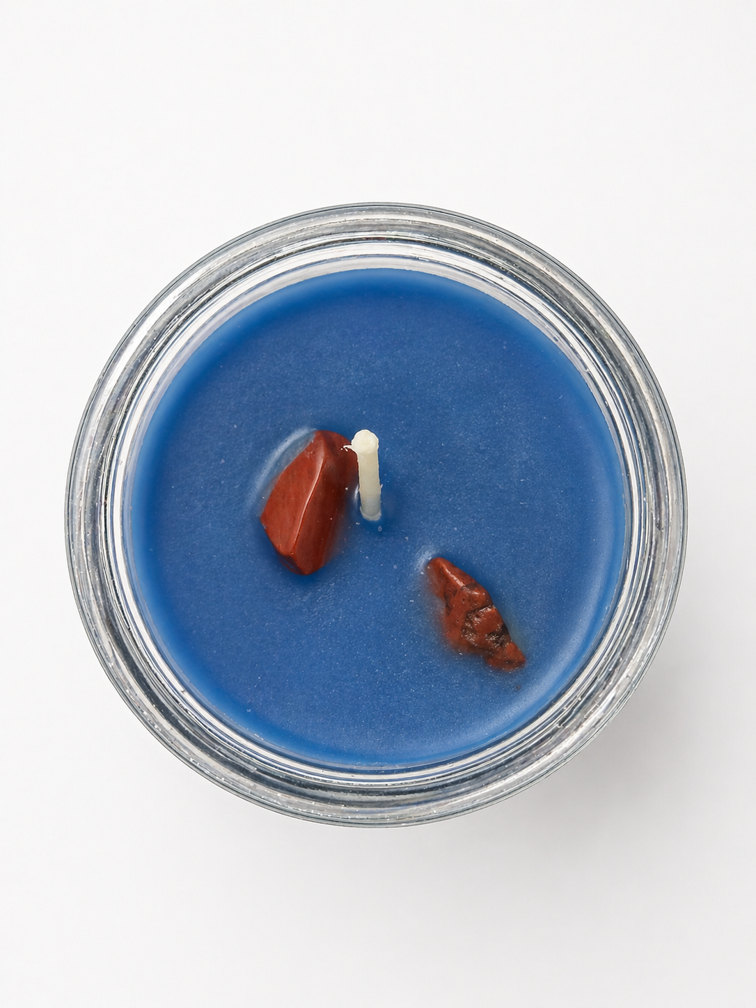 Blue candle in a glass jar with two small figurines on a white background