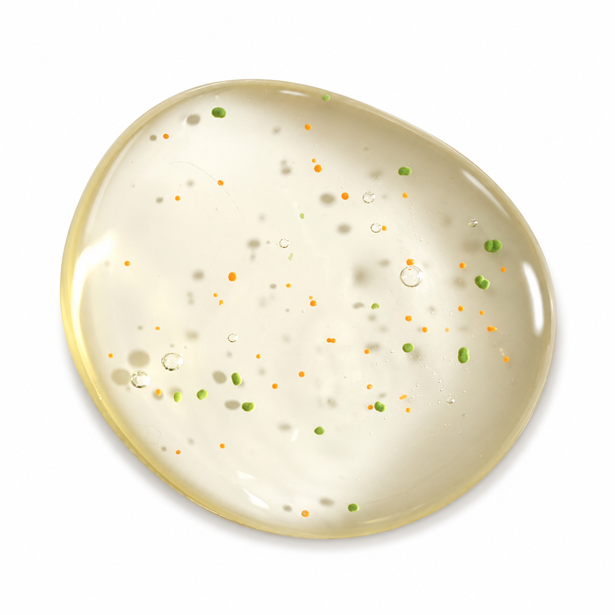 A translucent oval gel body wash patch with a pale yellow base and scattered tiny green and orange dots, shown on a plain white background.