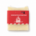 A handcrafted artisan soap bar wrapped in clear plastic with a red paper label that reads 'HANDCRAFTED ARTISAN SOAP' and 'Love Letter,' on a white background.