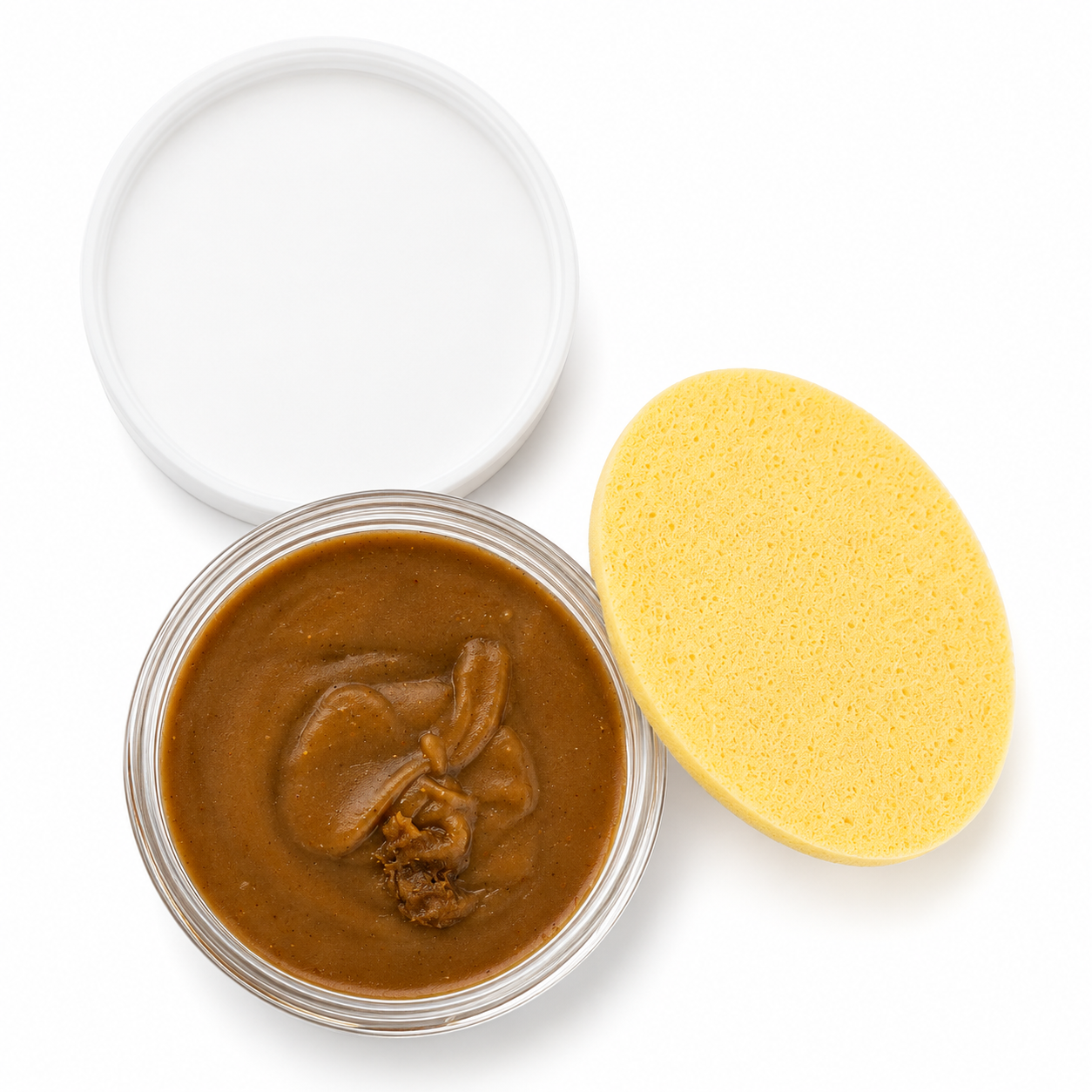 A clear round jar filled with thick brown soap, shown open with a white lid beside it and a yellow sponge on a white background.