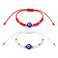 Two bracelets with red and white strings and blue evil eye beads on a white background
