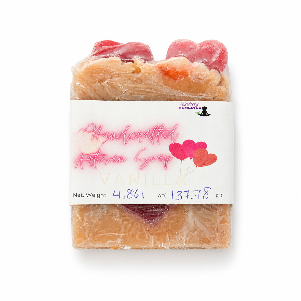 A handmade artisan soap bar wrapped in clear plastic with a white paper label. The label reads 'Handcrafted Artisan Soap VANILLA' with pink script and heart graphics.