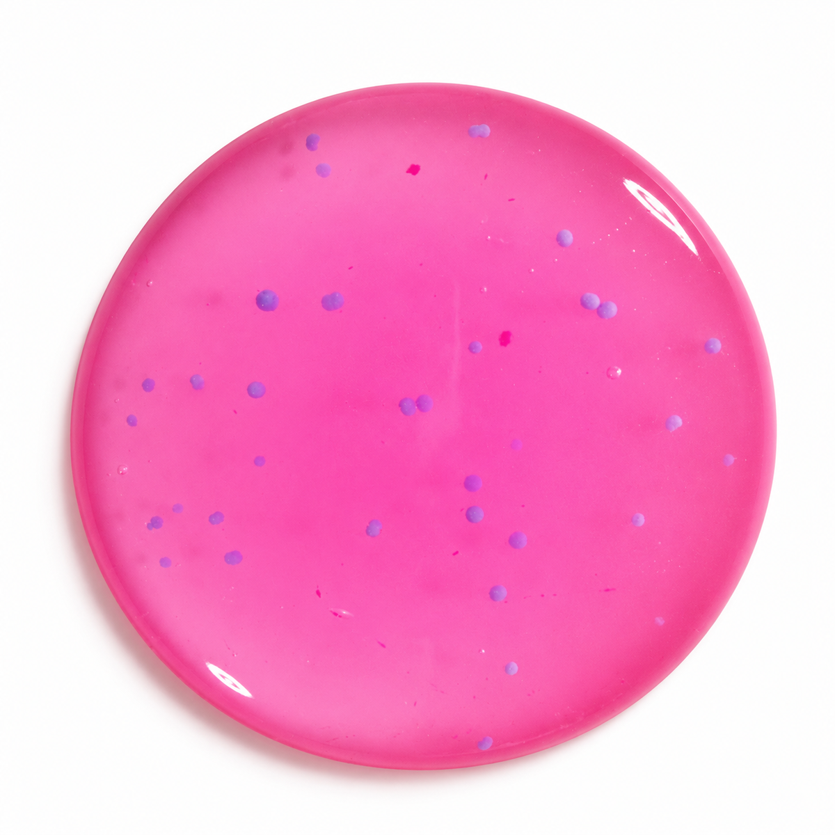 A circular, glossy pink body wash disc with embedded small blue jojoba beads shown on a plain white background.