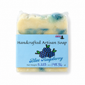 A packaged handmade soap bar labeled 'Blue Raspberry' with a light blue paper label, shown on a plain white background. The soap itself is visible through clear plastic wrapping and appears marbled in pale cream and blue-green tones.
