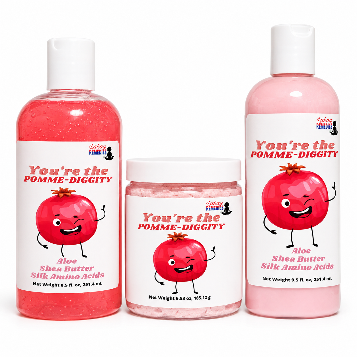 Three skincare products from Lakay Remedies on a white background: a pink bottle of Aloe Shea Butter Silk Amino Acids body lotion, a pink jar of body scrub, and a pink bottle labeled 'You're the POMME-DIGGITY' body wash.