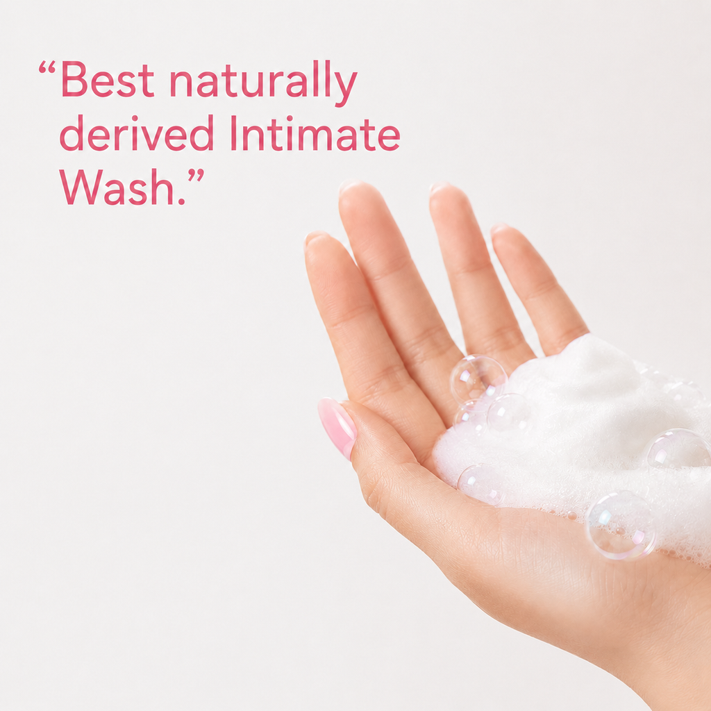 A hand with pink manicured nails holding white foam bubbles, with pink text in the upper left reading, “Best naturally derived Intimate Wash.”.