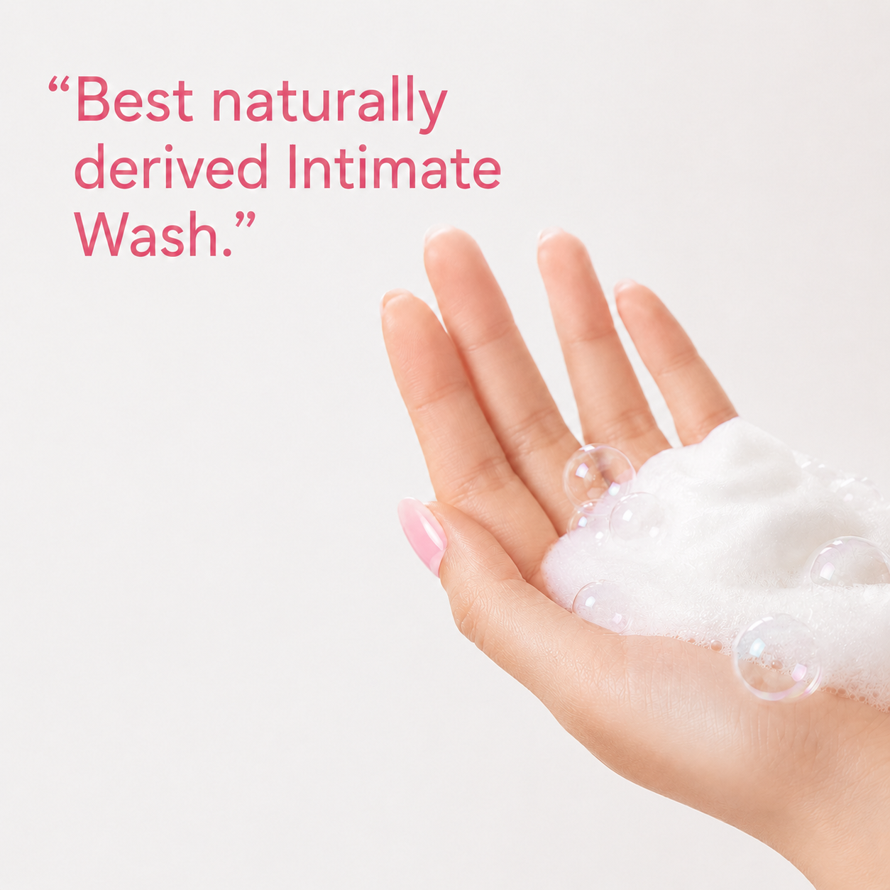 A hand with pink manicured nails holding white foam bubbles, with pink text in the upper left reading, “Best naturally derived Intimate Wash.”.