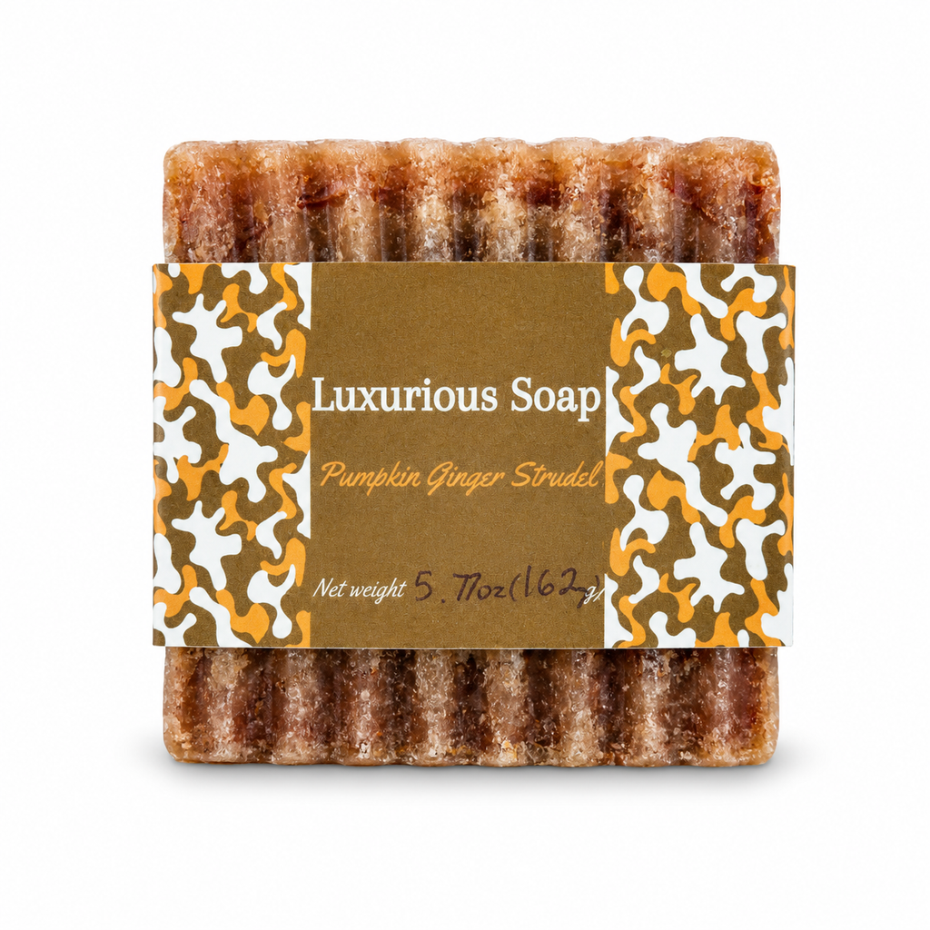 A single bar of Luxurious Soap 'Pumpkin Ginger Strudel' soap, showing its textured, brown, sugar-coated surface, wrapped in a brown paper label with orange and white camouflage patterns.