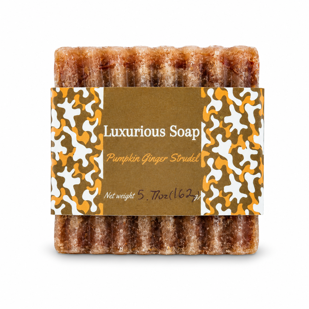 A single bar of Luxurious Soap 'Pumpkin Ginger Strudel' soap, showing its textured, brown, sugar-coated surface, wrapped in a brown paper label with orange and white camouflage patterns.