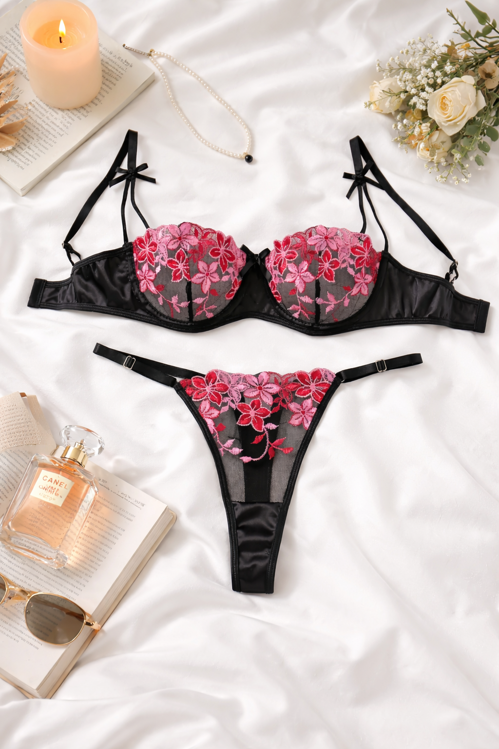 Black lingerie set with pink floral design on a white surface with candles and flowers.