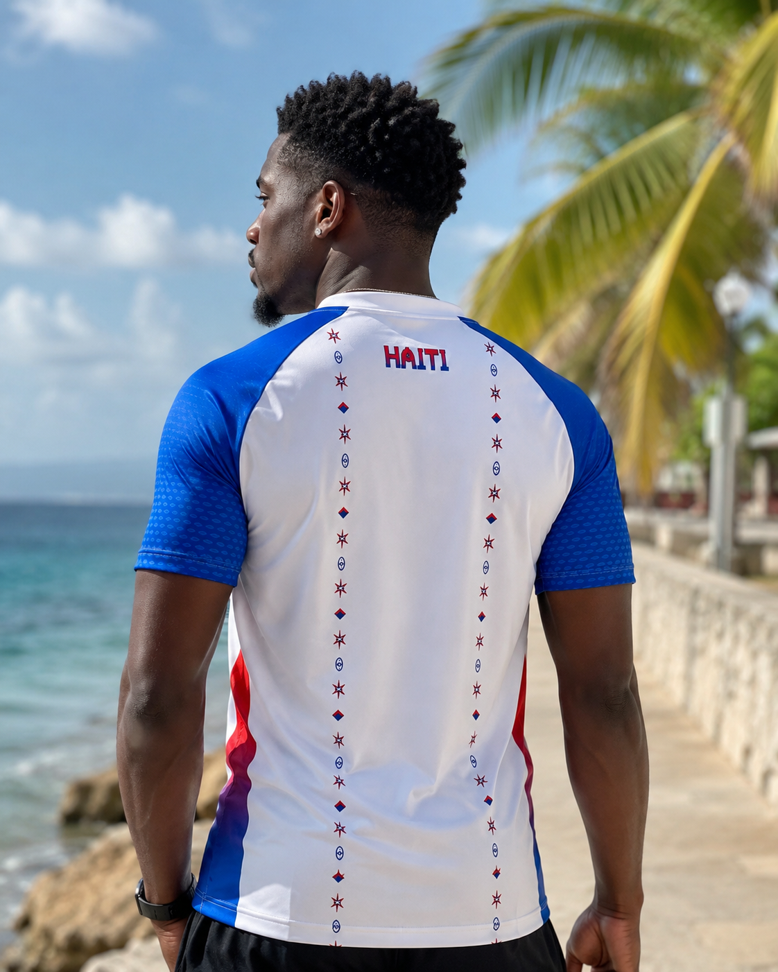 Man wearing a Haiti-themed shirt by the ocean with palm trees in the background