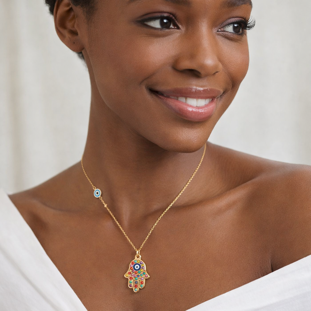 Woman wearing a gold necklace with a colorful hamsa pendant against a neutral background