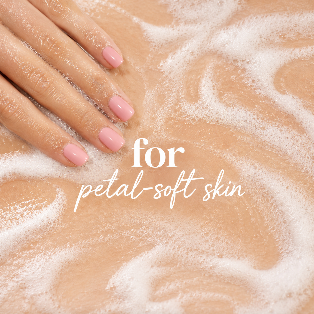 A close-up of a hand with pale pink manicured nails resting on a foamy beige surface, with the text 'for petal-soft skin' overlaid in white.