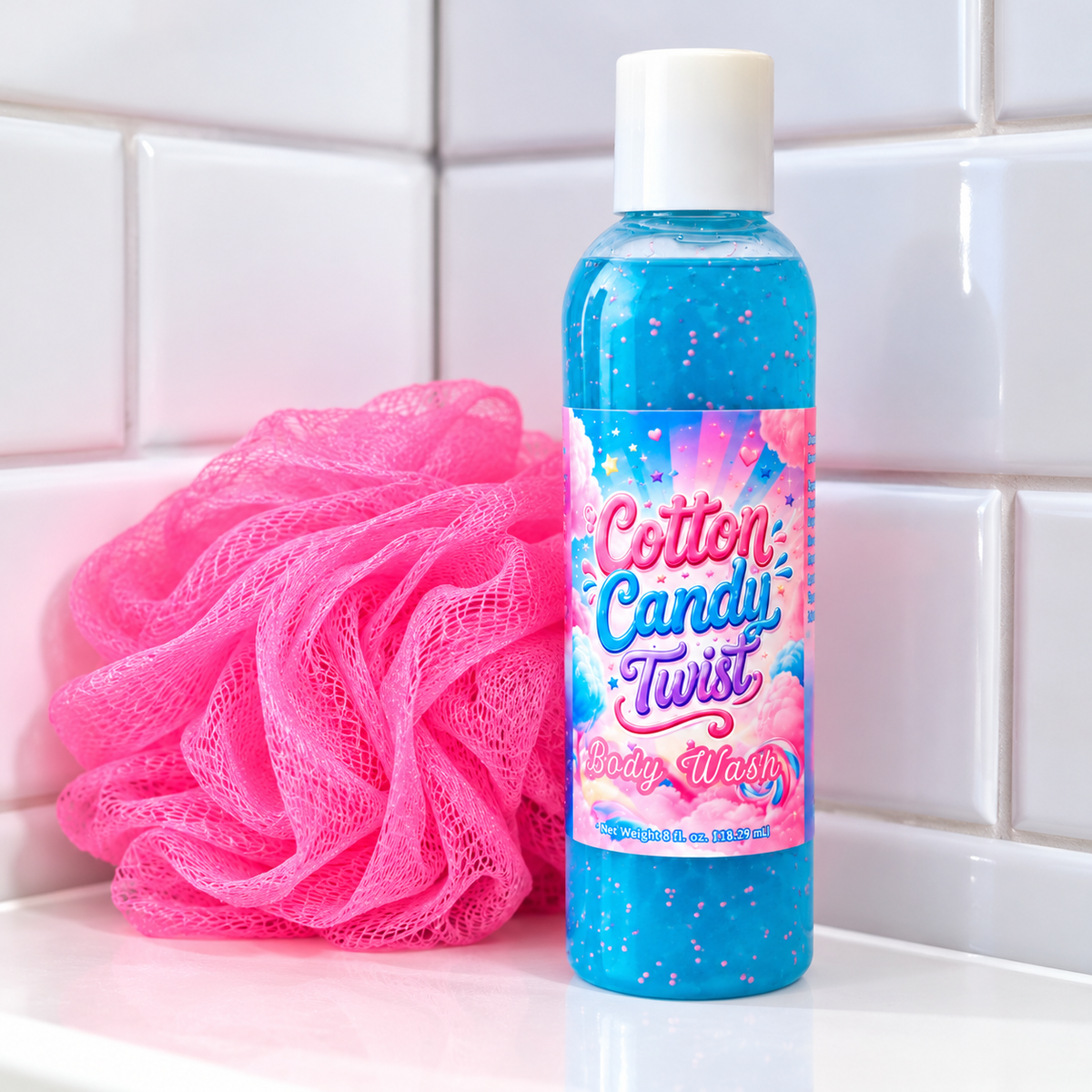 Cotton Candy Twist Body Wash in vibrant blue with pink exfoliating beads, displayed beside a bright pink bath loofah on a white bathroom countertop with a clean white tile background.