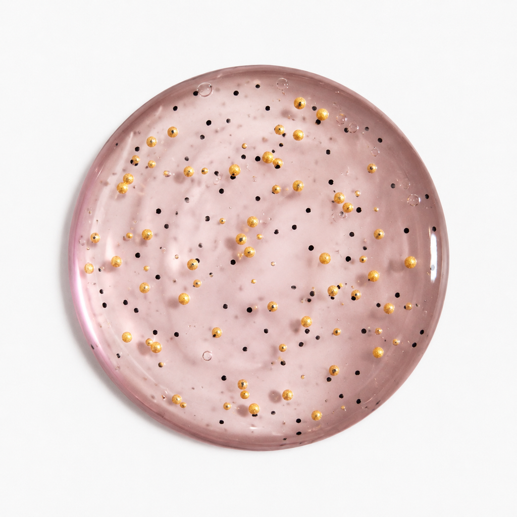 A round body washdish scattered small gold and black jojoba beads, shown from a top-down view on a clean white background.