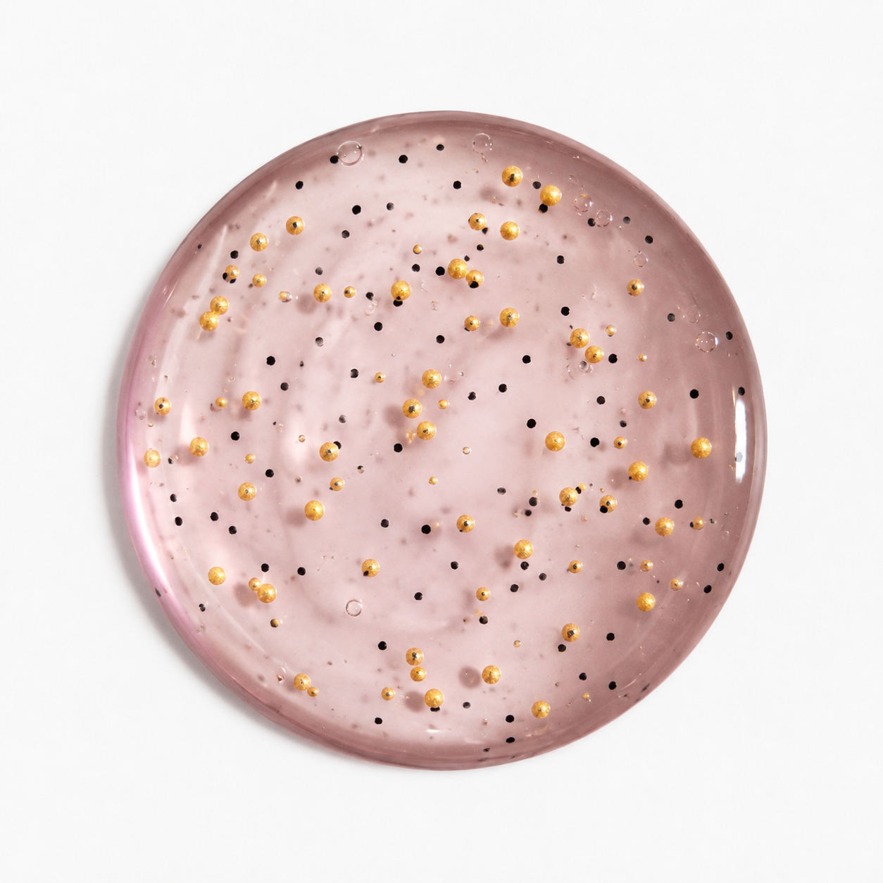 A round body washdish scattered small gold and black jojoba beads, shown from a top-down view on a clean white background.